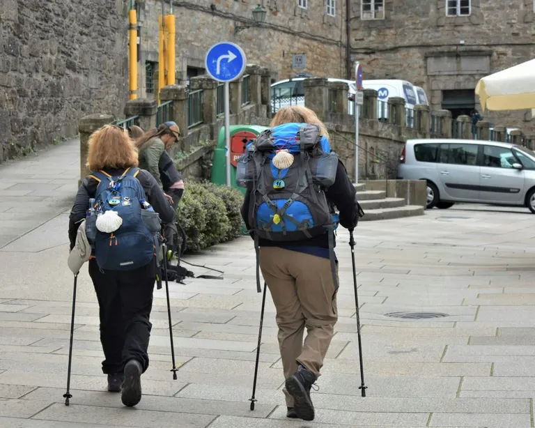 Zwei Wanderer mit grossen Rucksäcken und Stöcken gehen durch eine gepflasterte Stadtstrasse.