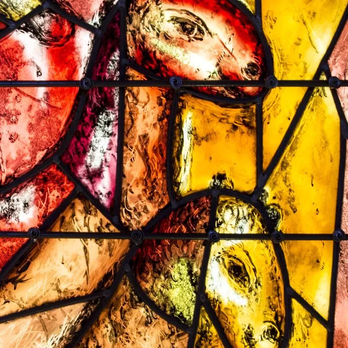 A colorful stained-glass window featuring stylized horse heads, predominantly in shades of red, yellow, and brown.