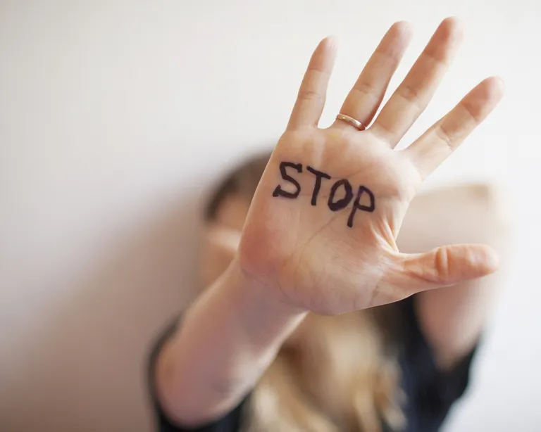Eine Person hält ihre Hand mit dem Wort «STOP» darauf geschrieben in die Kamera, Gesicht unscharf im Hintergrund.