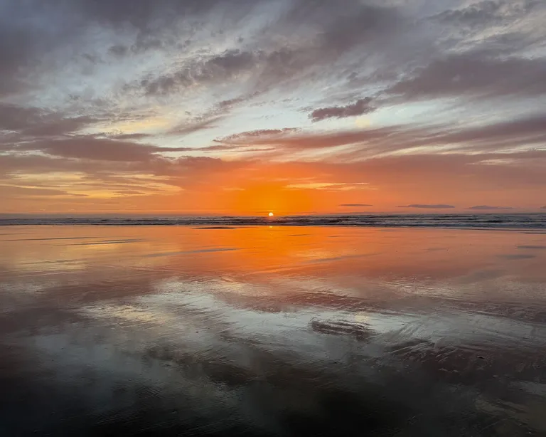 Sonnenuntergang über einem ruhigen See, der Himmel und das orange Licht spiegeln sich im Wasser.