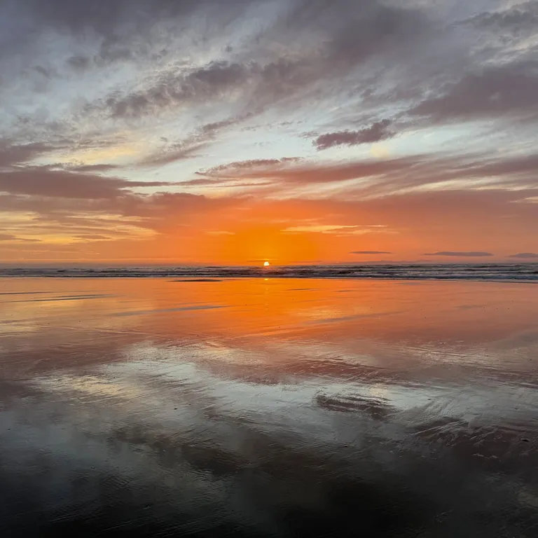 Sonnenuntergang über einem ruhigen See, der Himmel und das orange Licht spiegeln sich im Wasser.