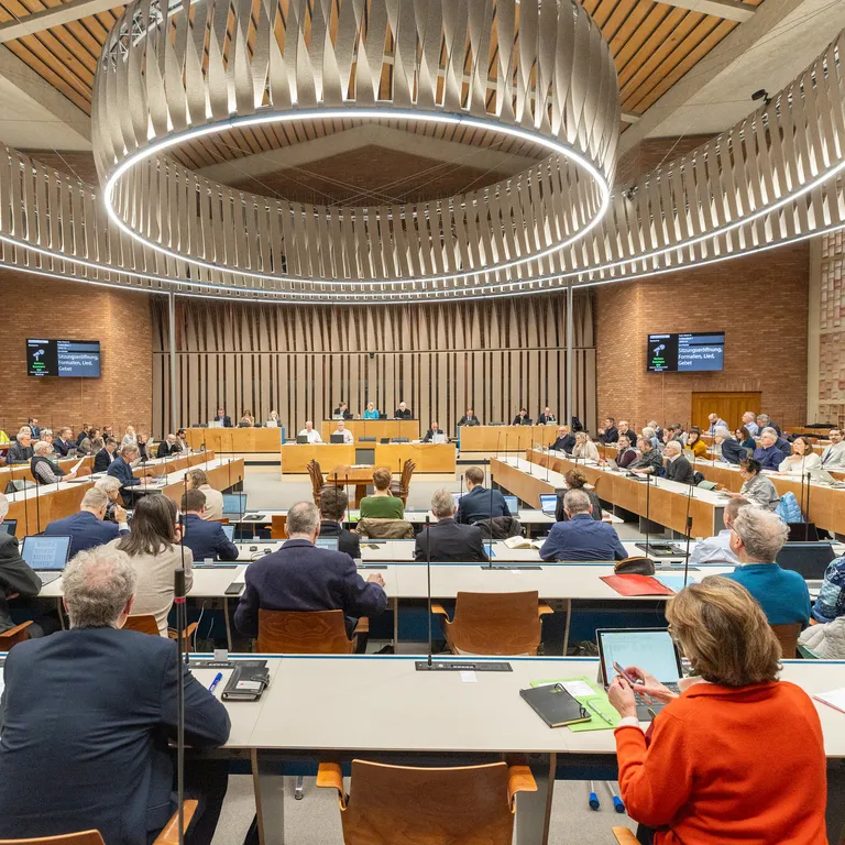 Großer Konferenzsaal, viele Menschen sitzen an Tischen und hören einem Vortrag oder einer Diskussion zu.