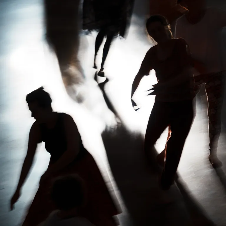 Mehrere tanzende Personen werfen lange Schatten auf einen beleuchteten Boden.