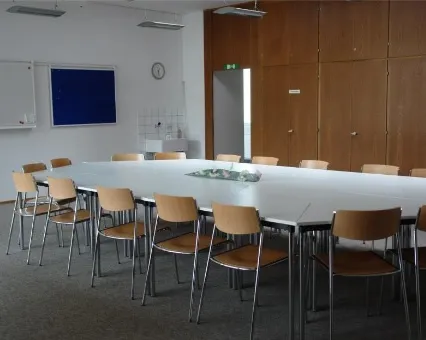 Konferenzraum mit grossem, U-förmigem Tisch, Holzstühlen, Whiteboard und Glastür, modern und hell eingerichtet.