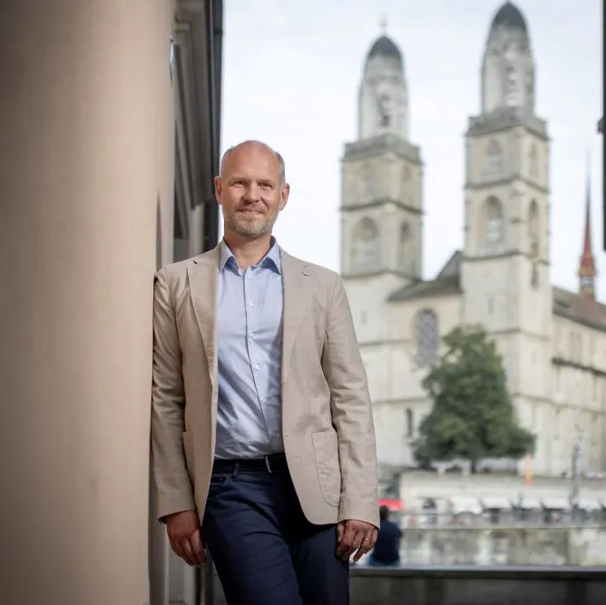 Pfarrer Christian Walti steht lächelnd draussen, im Hintergrund ist das Zürcher Grossmünster zu sehen.