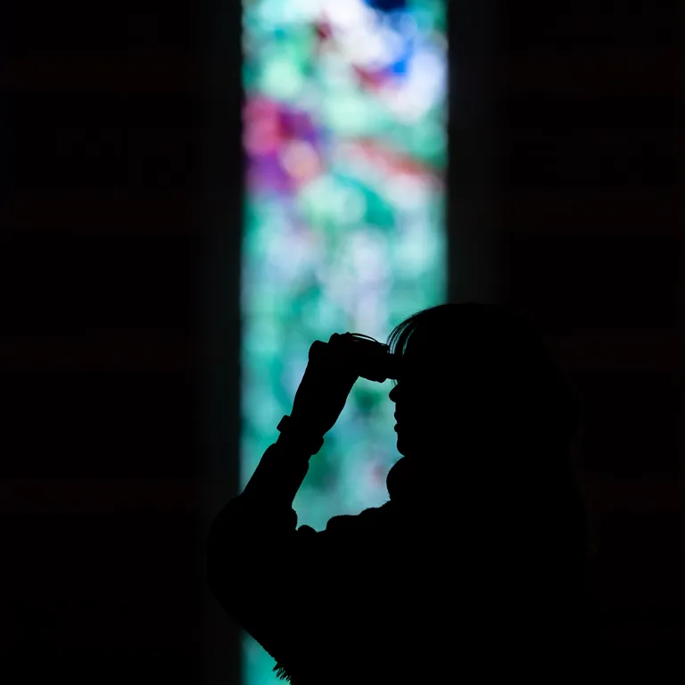Schattenriss einer Person vor bunten, unscharfen Kirchenfenstern mit abstrakten Mustern.