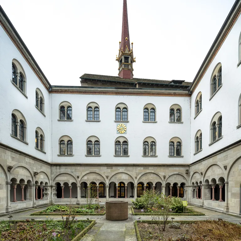 Kreuzgang des Grossmünsters mit Rundbögen, Gartenanlage und einem Kirchturm im Hintergrund.