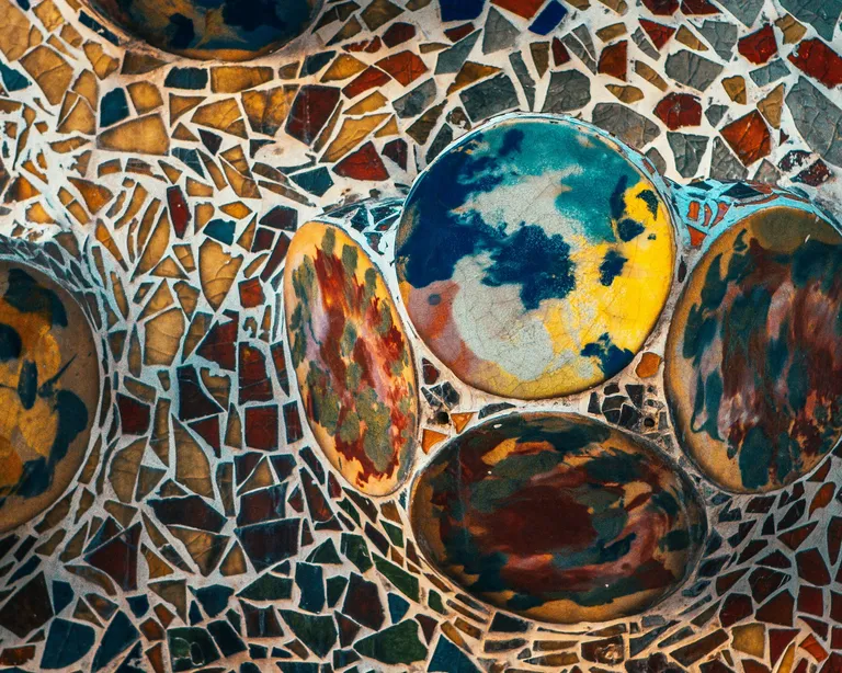 Mosaik aus bunten Fliesen mit runden, gemusterten Elementen in Blau, Gelb und Rot auf unregelmäßigem Hintergrund.
