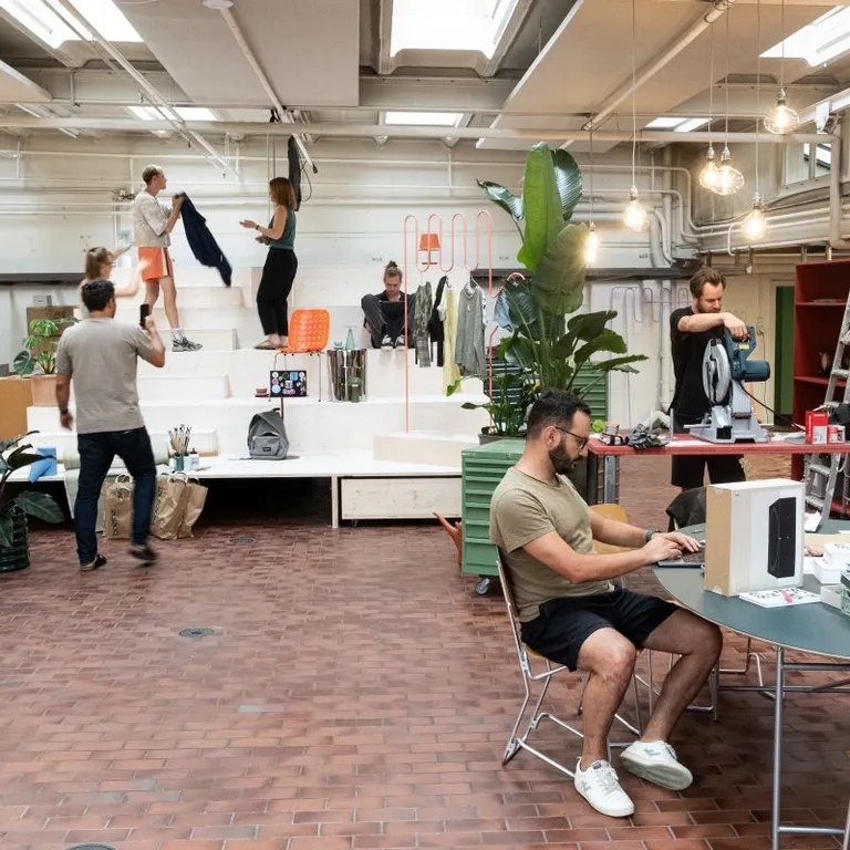 Mehrere Menschen arbeiten und unterhalten sich in einem modernen, offenen Büro mit Pflanzen und Licht von oben.