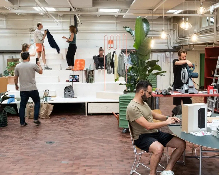 Mehrere Menschen arbeiten und unterhalten sich in einem modernen, offenen Büro mit Pflanzen und Licht von oben.