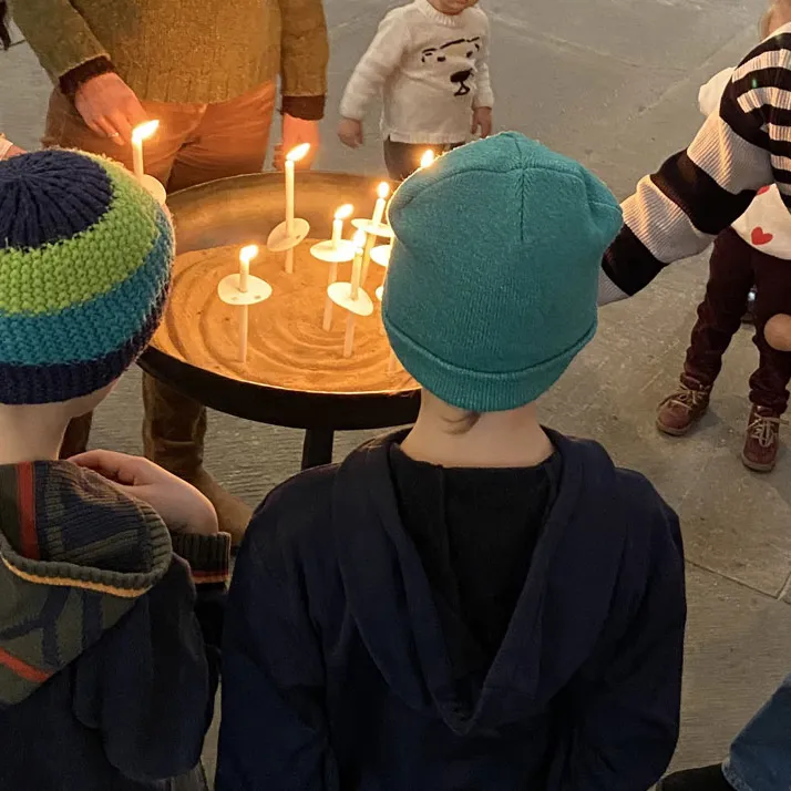 Mehrere Kinder stehen um einen Tisch mit brennenden Kerzen und sehen auf das Kerzenlicht.