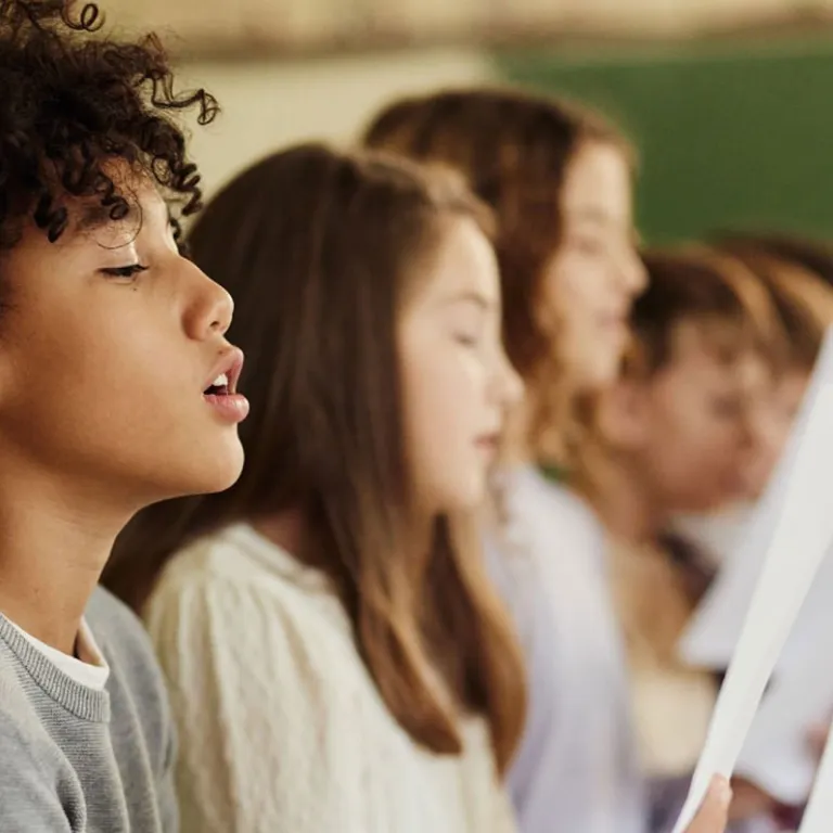 Mehrere Kinder sitzen nebeneinander und singen, während sie Notenblätter in den Händen halten.