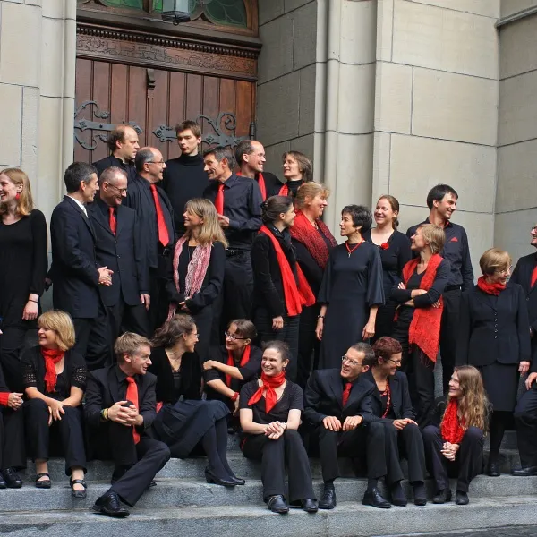 Eine größere Gruppe von Menschen in schwarzer Kleidung mit roten Akzenten steht und sitzt auf Treppen vor einem Gebäude.